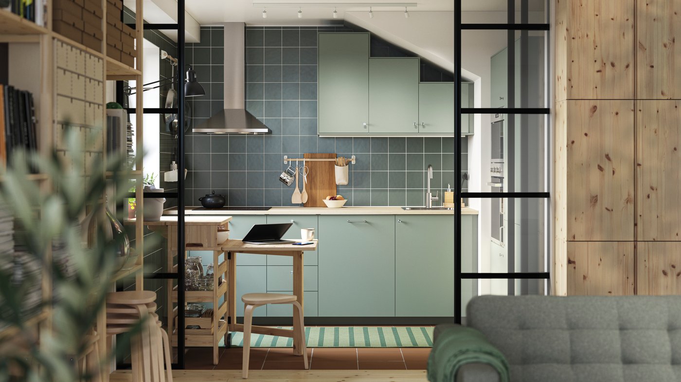 A green L-shaped kitchen has grey green NICKEBO fronts and a RESARÖ mobile drop-leaf table with storage and some stools.