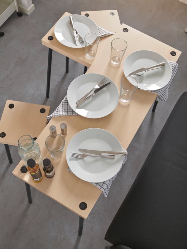 In a dorm room, two FRIDNÄS nesting tables and FRIDNÄS stools are set up for a simple dinner party for four people.