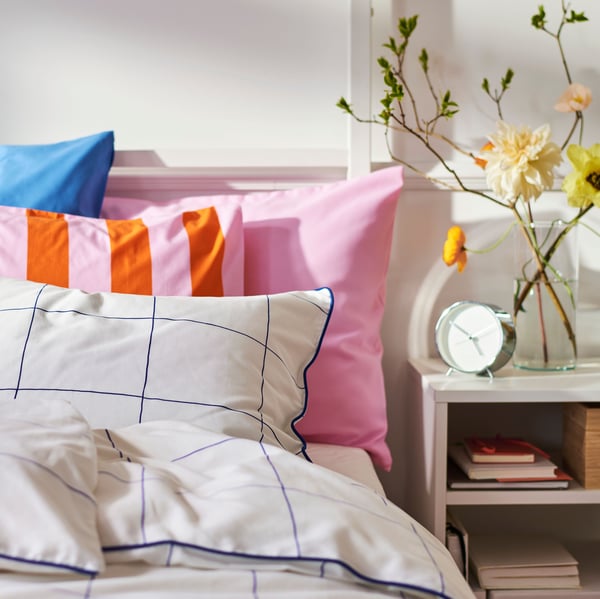 Close-up of bed with a lot of pillows in different patterns and colours. Bedside table on the right.