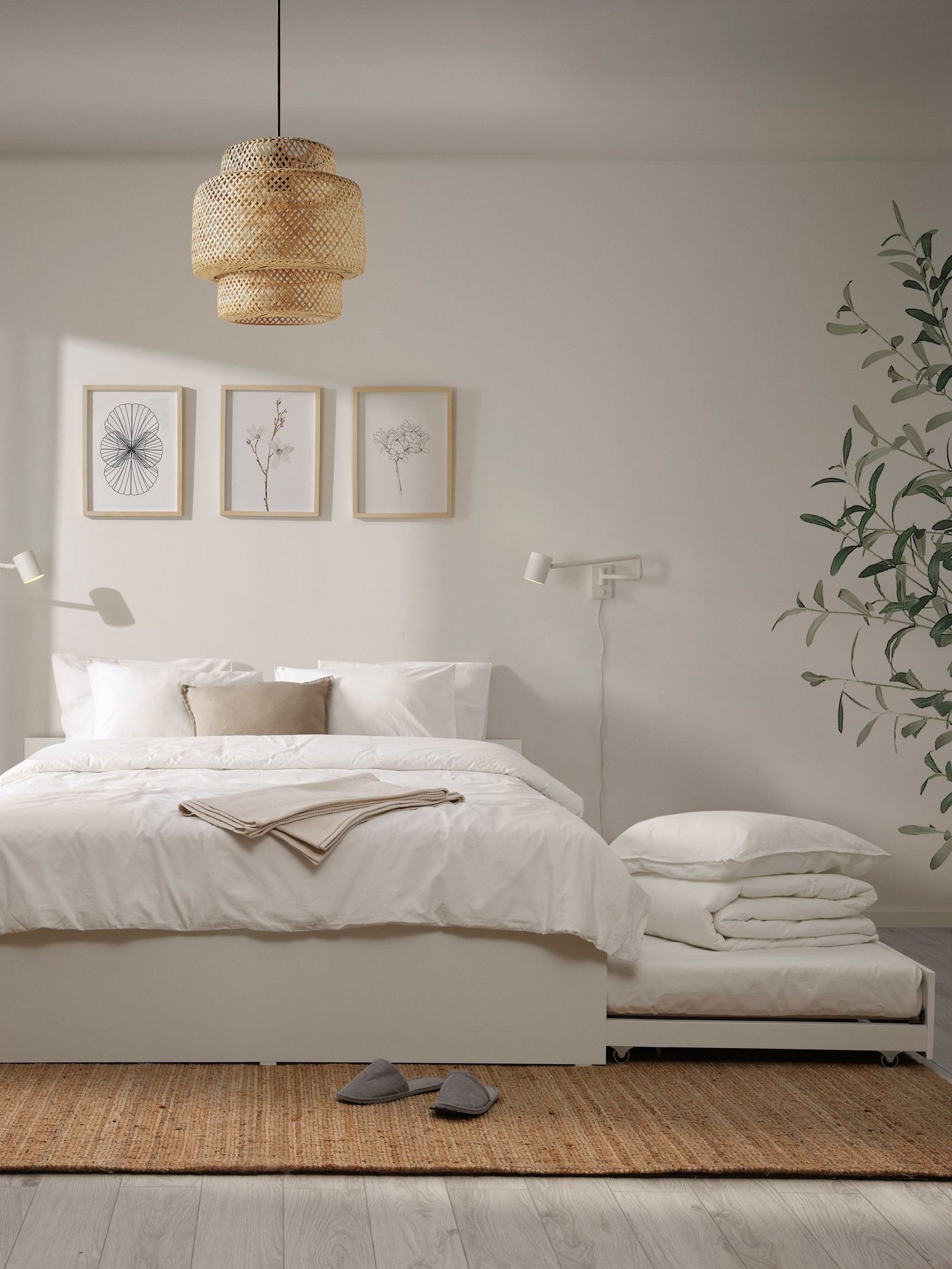 A white VIHALS bed with trundle bed underneath it. A white NYMÅNE wall lamp above the bed.