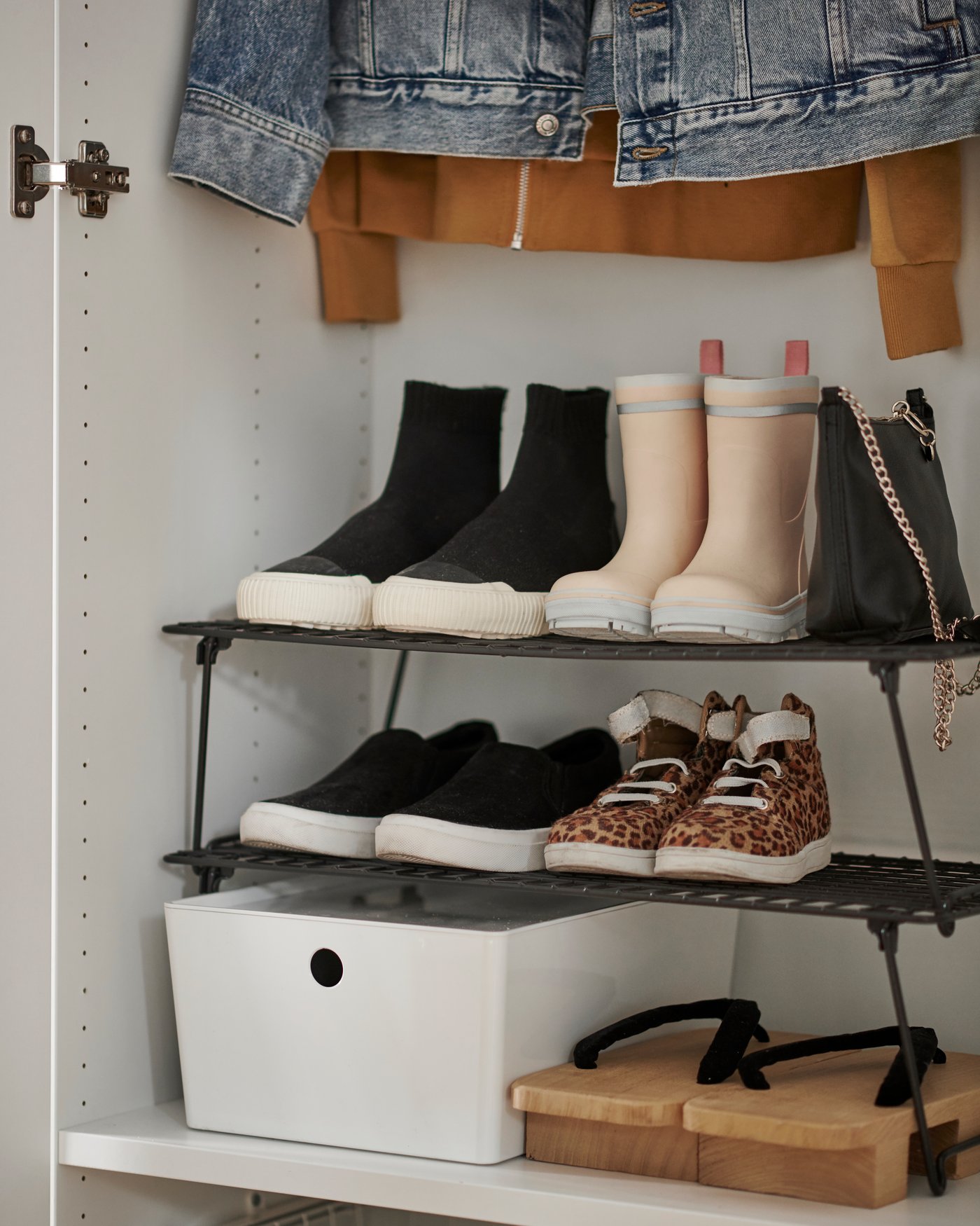 Section of a wardrobe cabinet in which a full GREJIG shoe rack stands amid other clothes and accessories.