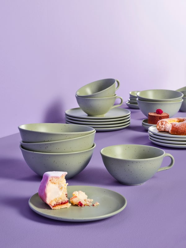 Several MOSSMAL side plates, bowls and mugs on a lilac surface. There are leftover desserts on some of the plates. 
