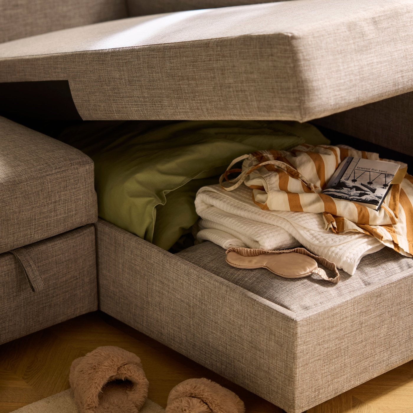 The gaping chaise-longue part of a FRIHETEN sofa-bed, revealing bedding and textiles placed in the compartment within.