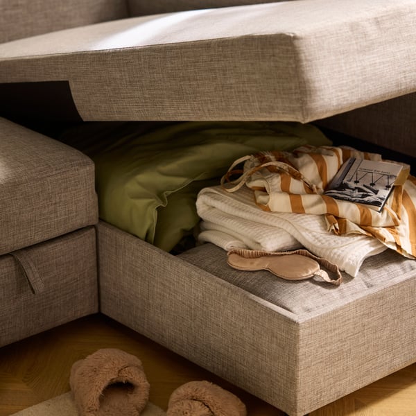 The gaping chaise-longue part of a FRIHETEN sofa-bed, revealing bedding and textiles placed in the compartment within.