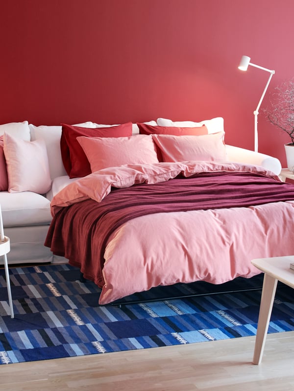 Living room with GRÖNLID sofa-bed  expanded to form a double bed, neatly made with fluffy bed textiles and cushions.
