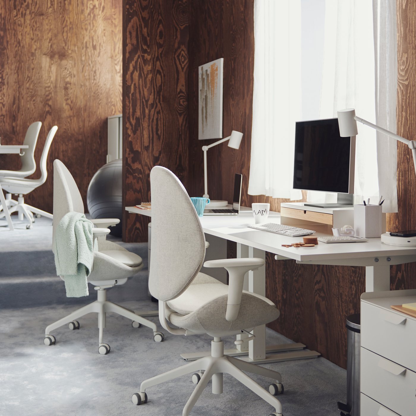 Workspaces with white TROTTEN desks and HATTEFJÄLL and LÅNGFJÄLL office chairs in a carpeted, brown, wood-panel office.