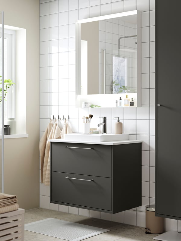 Un mobile per bagno HAVBÄCK con cassetti, grigio, un lavabo a semincasso ORRSJÖN e un mobile a specchio su una parete con le piastrelle.