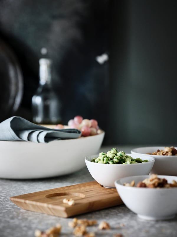 A TYNGDLÖS tray with three bowls filled with snacks on a terrazzo-style worktop. A white RUNDLIG serving bowl stands nearby.