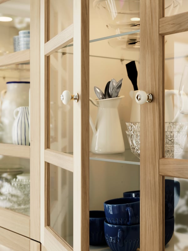 Krupan kadar vitrine s FORSBACKA frontovima, KLINGSTORP ručicama i nekoliko šolja i priborom za jelo u njoj.
