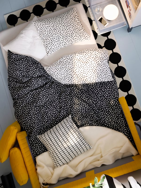 FRIDHULT sofa ležaj, konfigurisana kao ležaj, s BJÖRKGRÅMAL posteljinom i prljavobelim KLIPPOXEL tankim ćebetom, nalazi se na tepihu.