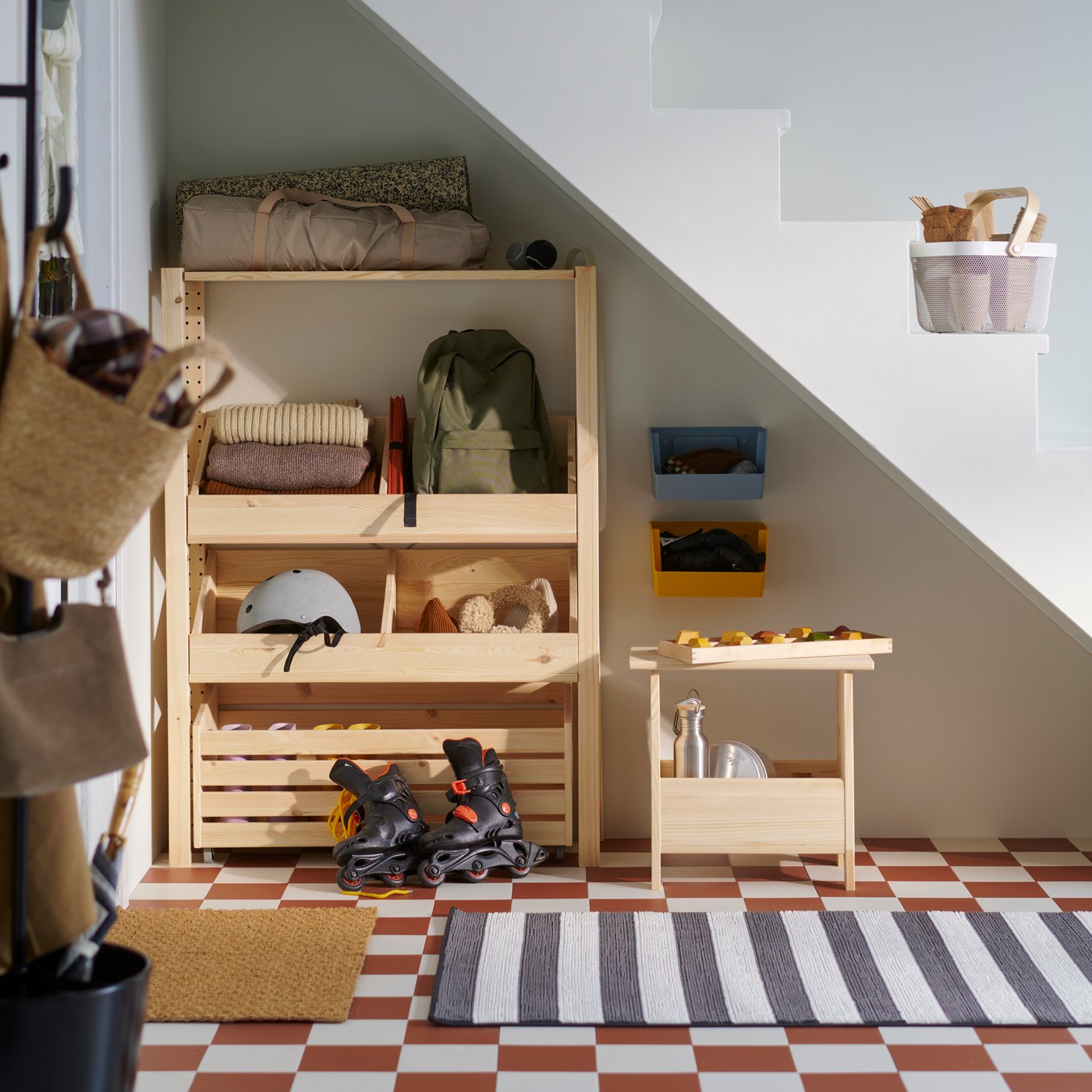 A hallway with a wooden IVAR box shelves holding helmets, bags and clothes, alongside shoes and a small table.