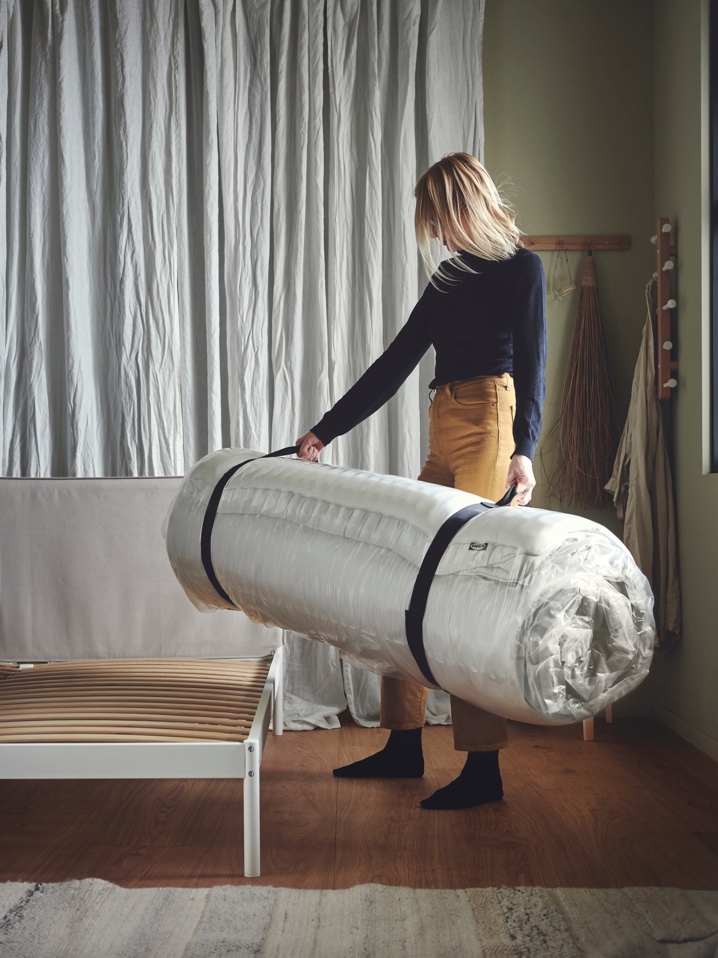 Une personne pose un tapis roulé sur un banc en bois dans une pièce au style intérieur calme et contemporain.