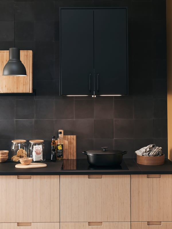 A kitchen cooking area with METOD cabinets, a black HEKTAR lamp and an induction cooking hob.