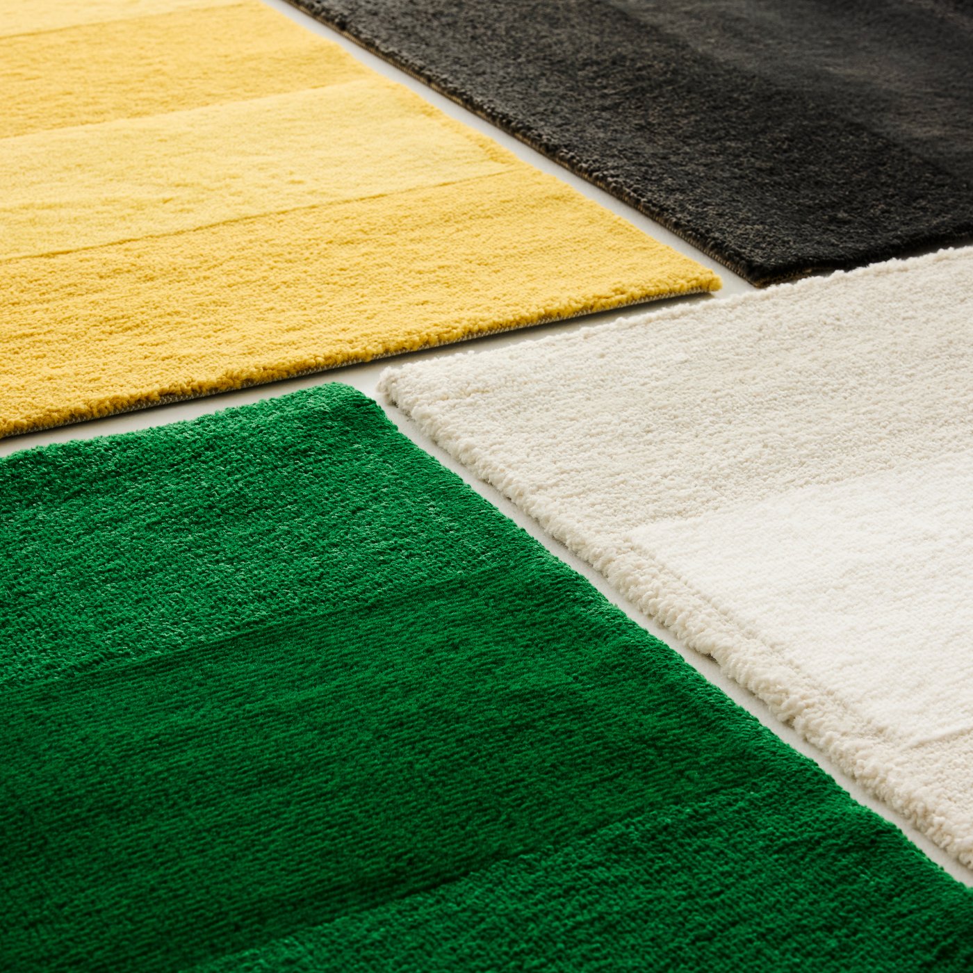 Close-up of four LANDSVÄG rugs, each in a different colour: green, white, yellow and black.