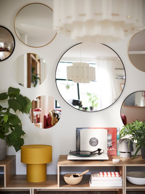 A large LINDBYN mirror with a black frame and other mirrors are attached to a wall above some HOLMERUD coffee tables.