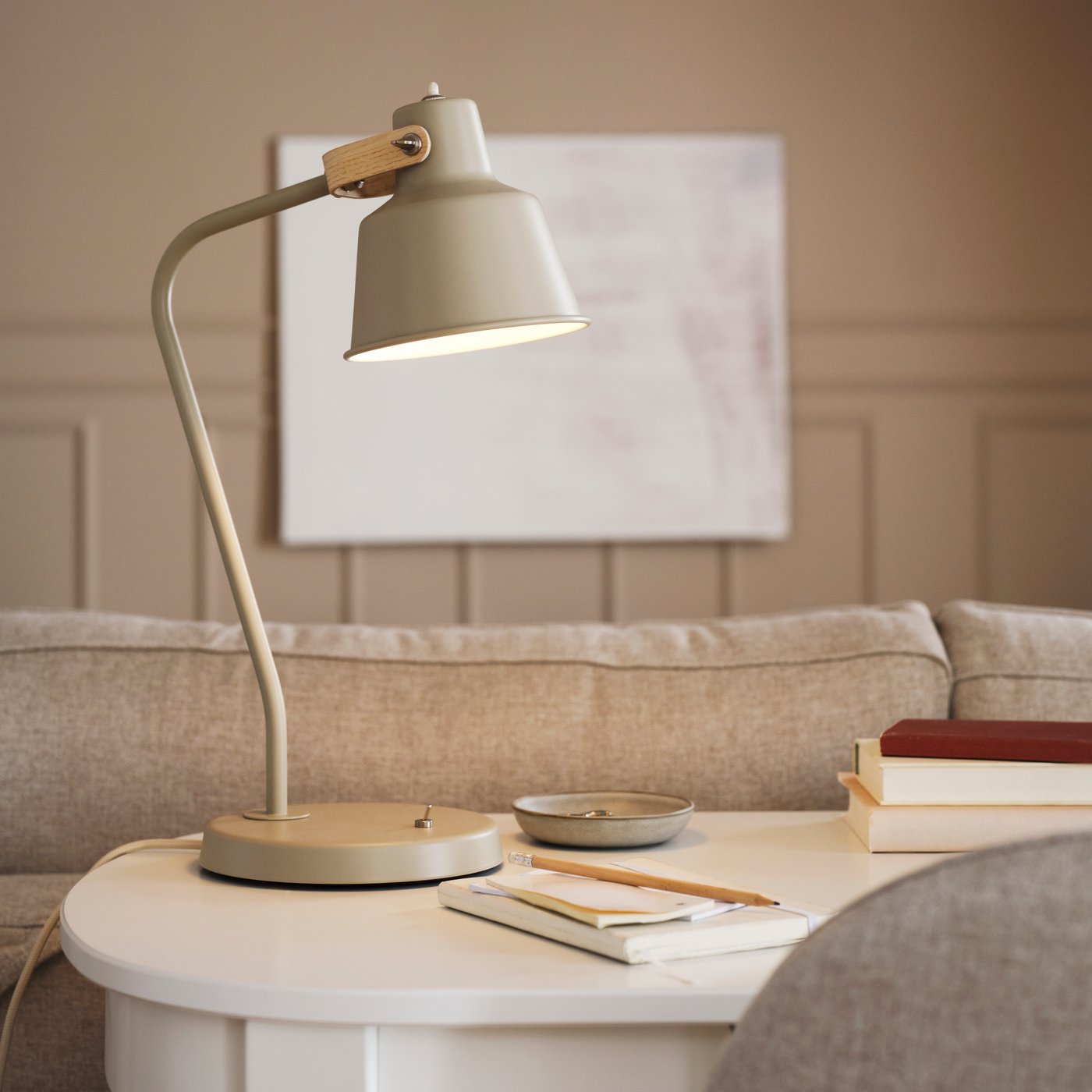 A beige/ash SJÖMAKT desk lamp stands on top of a white ROSENTORP desk along with a pencil and a notebook.