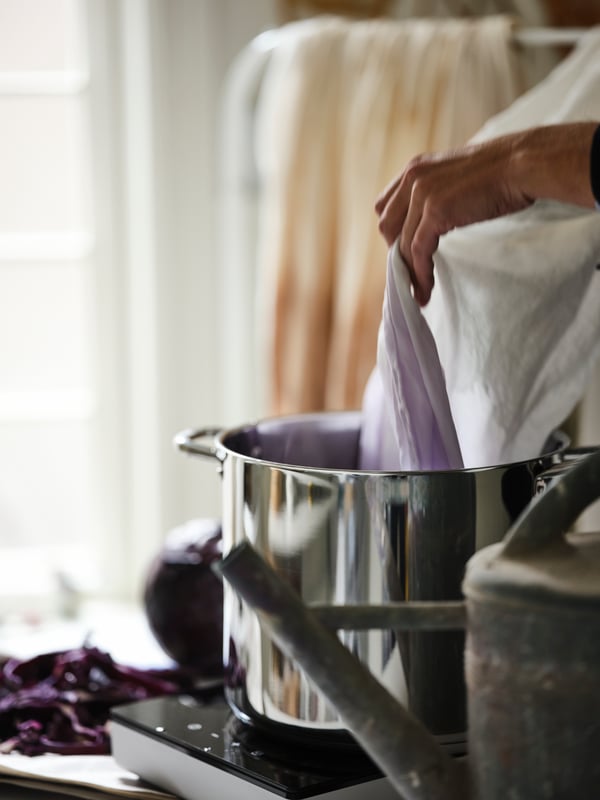 A length of white HANNALILL fabric being lowered into an IKEA 365+ stockpot on a white TILLREDA portable induction hob.