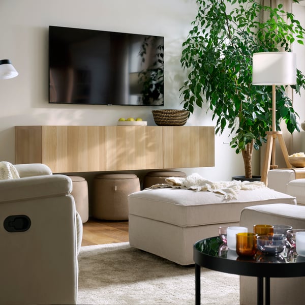 A light, bright living room with a KIVK pouffe, a SKULNÄS recliner, a STOENSE rug, a wall-mounted TV and a big, leafy plant.