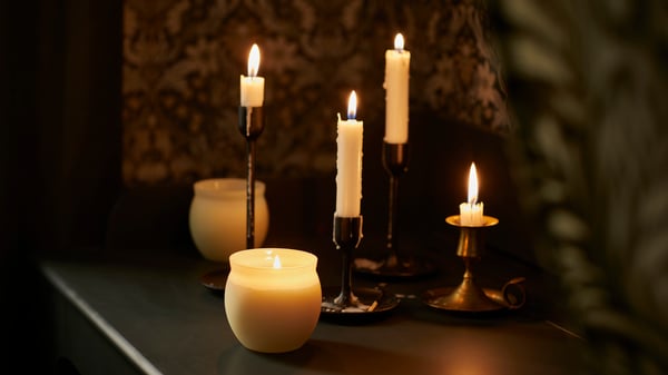 Four lit white dinner candles in gold candlesticks next to two scented candles in white glass holders.