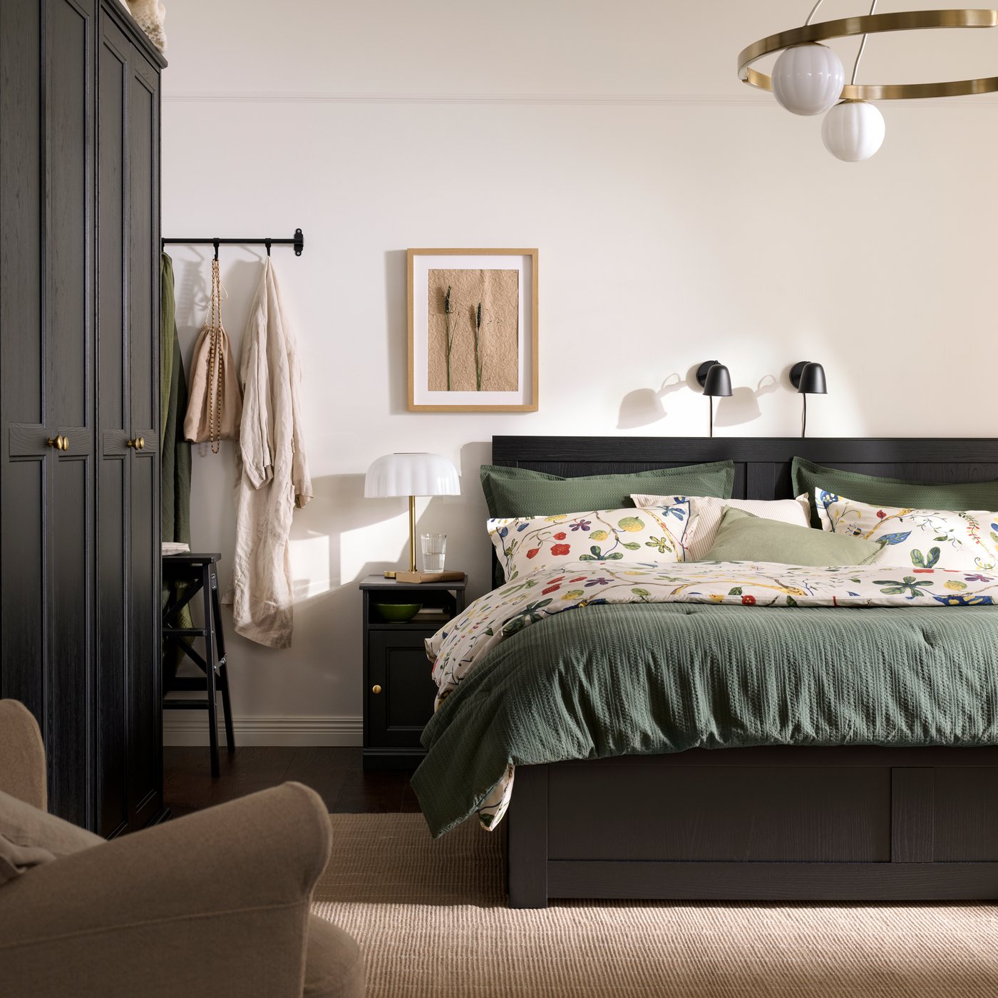 Una recámara de estilo tradicional con cama FÅGELFJÄLLET negra, buró y clóset a juego, y ropa de cama verde con motivos florales.