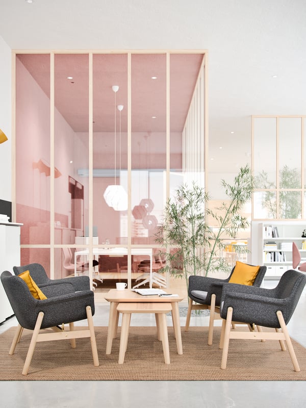 Office meeting space with four chairs around a nest of coffee tables with a cup and papers on top and plants.