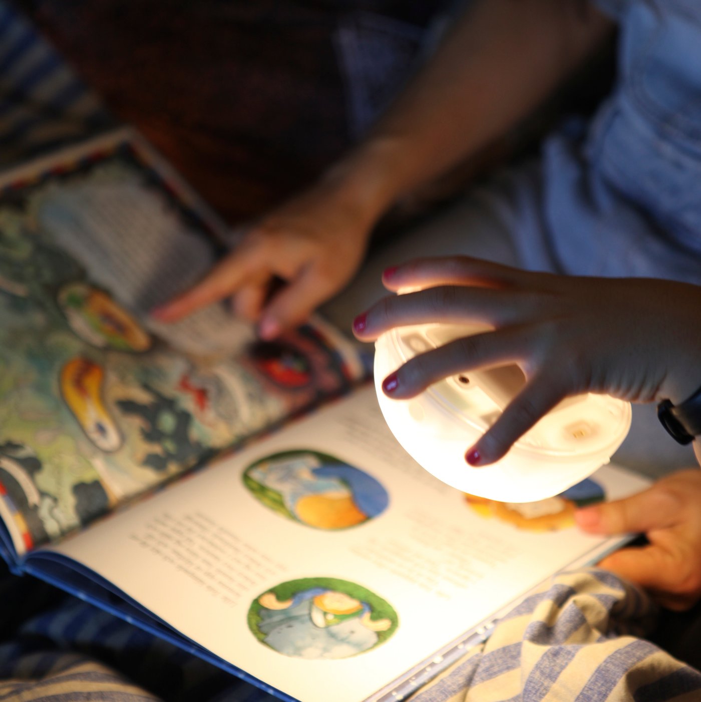 Tangan seseorang memegang sumber cahaya lampu meja berkuasa solar LED SAMMANLÄNKAD pada beberapa halaman buku gambar.