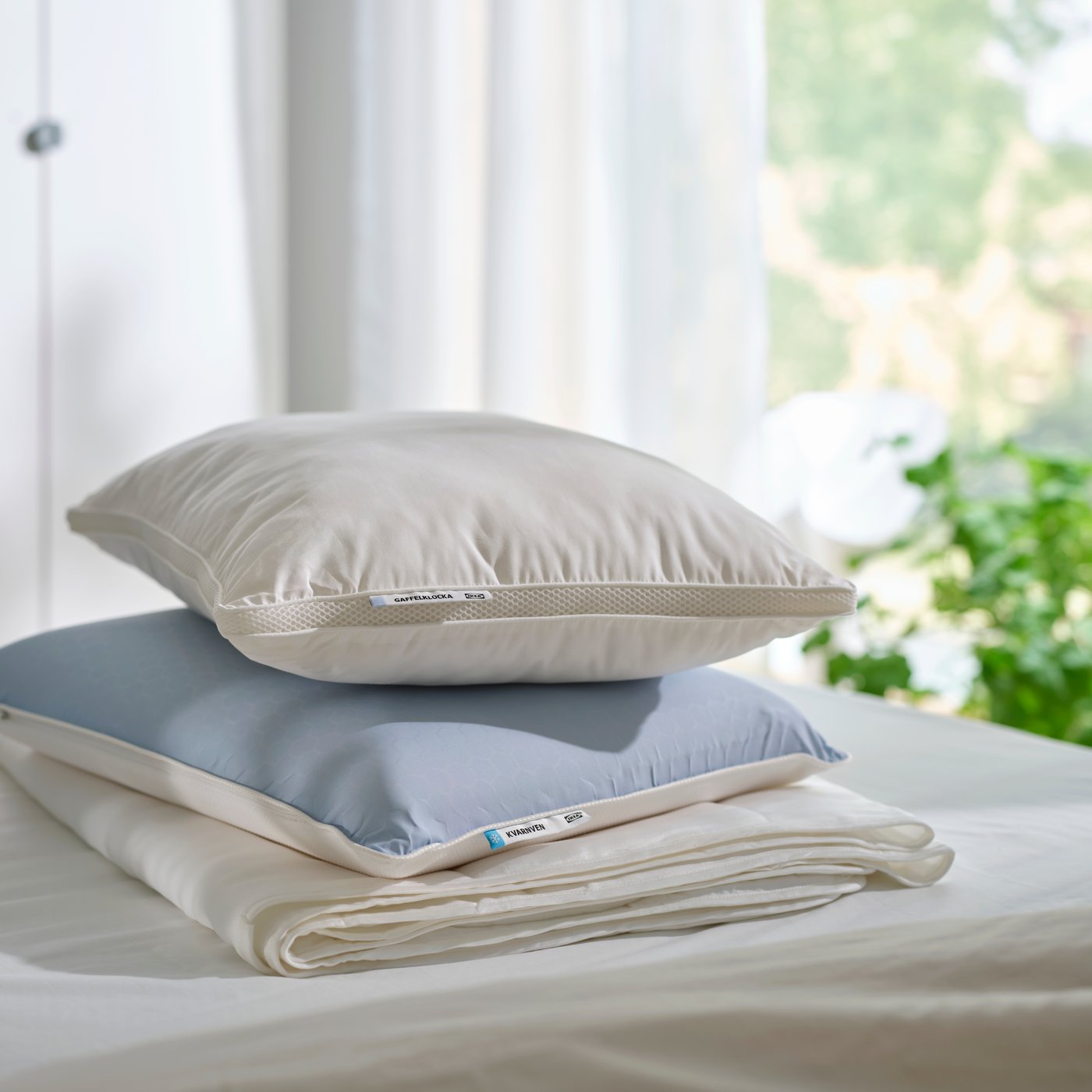 A GAFFELKLOCKA pillow and KVARNVEN ergonomic pillow are stacked on top of a duvet on a bed.