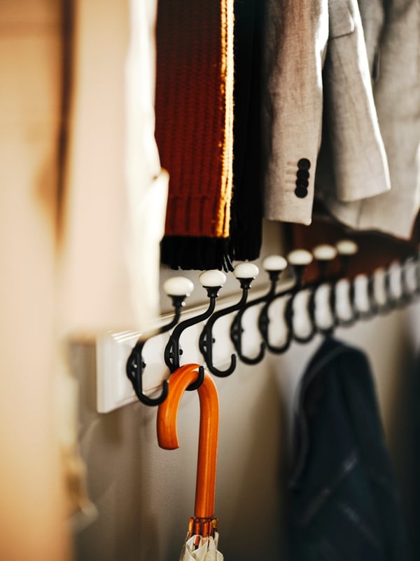 An umbrella and denim jacket hanging from a few white LANDKRABBA racks with 5 hooks with jackets hanging above.