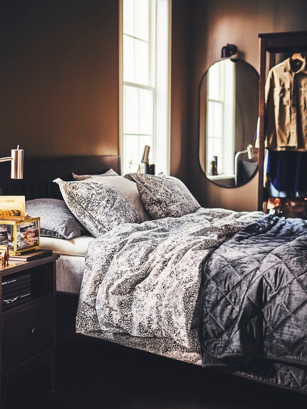 Una recámara con un juego de cama ÄNGSKLOCKA, una cama IDANÄS con barniz café oscuro y un buró con un espejo LINDBYN negro.