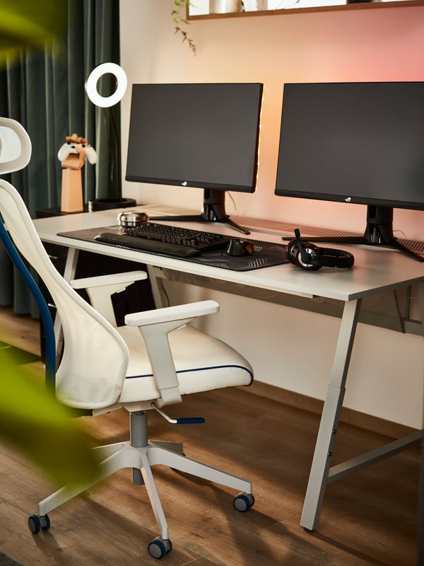 An UTESPELARE gaming desk and a white MATCHSPEL gaming chair in a home workspace with two computer monitors.