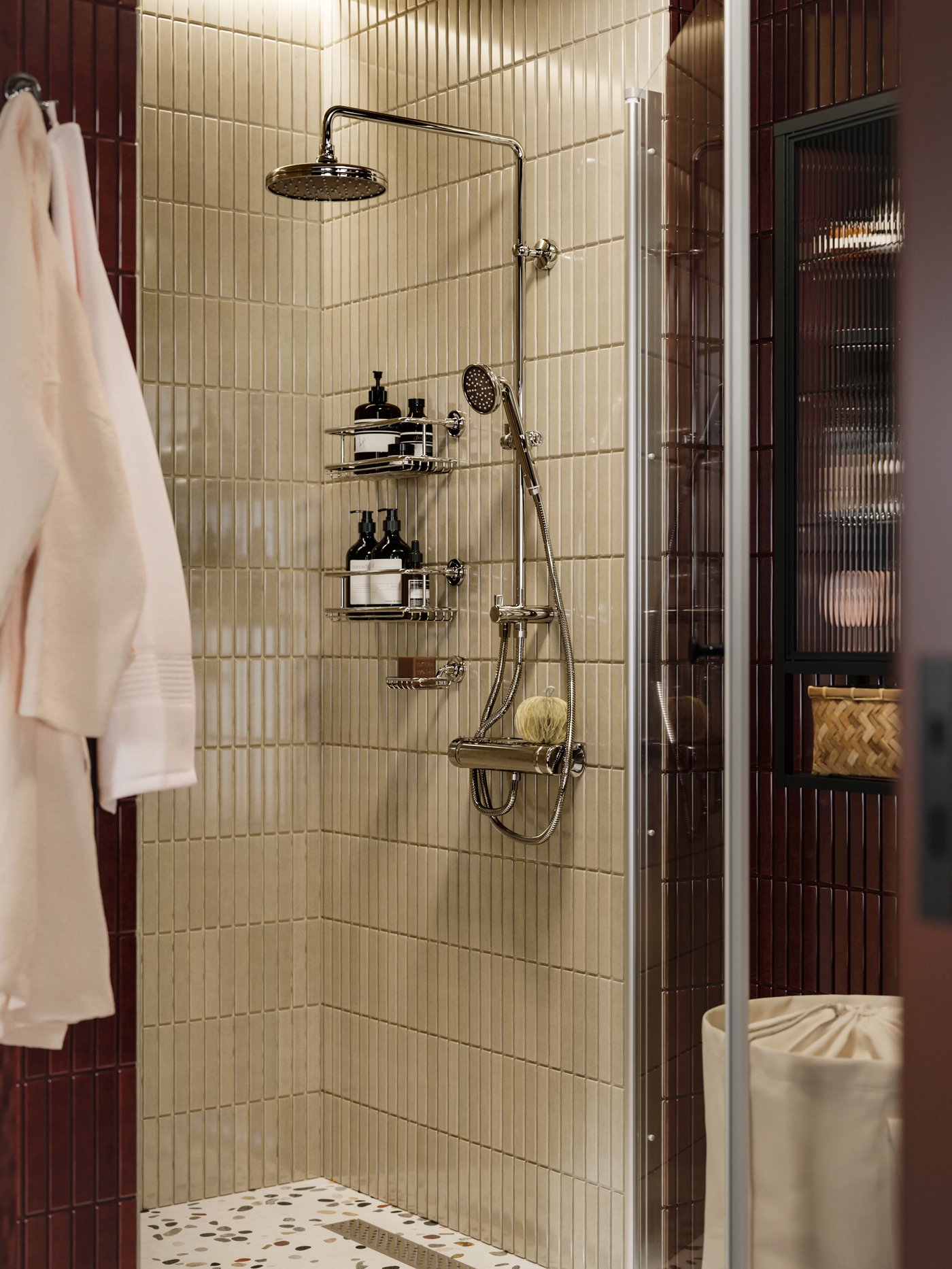 Salle de bain avec ensemble douche/mitigeur VOXNAN avec déviateur, carreaux beiges et structure de rangement chargée d’articles de toilette et d’une éponge.