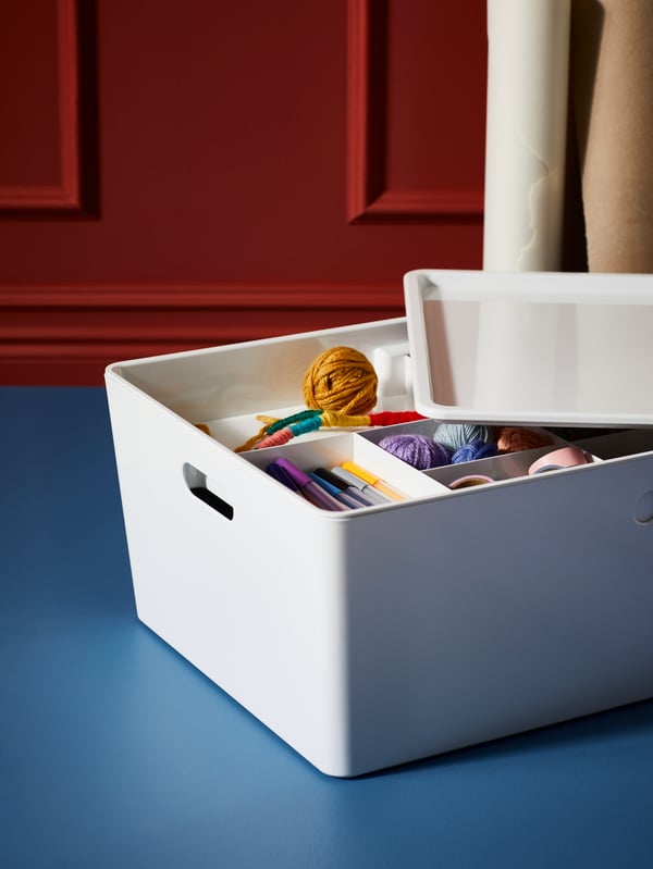 A white KUGGIS box with the lid partly off, revealing a KUGGIS insert with its compartments filled with crafts accessories.