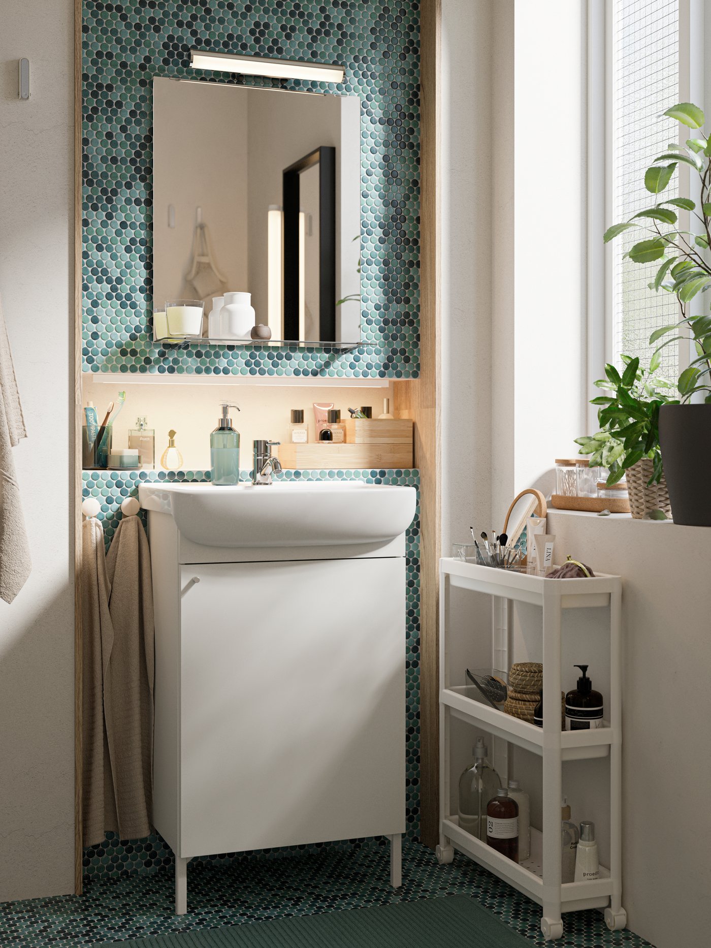 White NYSJÖN wash-basin cabinet with mirrored wall cabinet next to a white VESKEN trolley with bathroom accessories and plants.