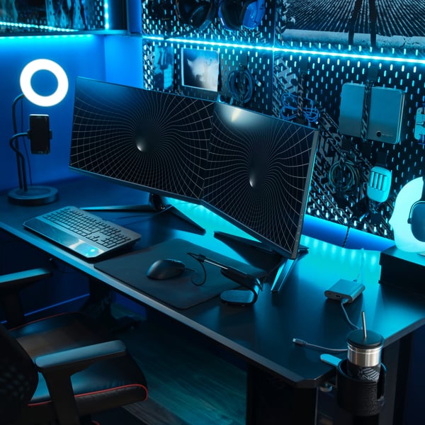 Mug with a lid and a straw holder attached to a computer gamer’s black desk with headphones in the blue background.