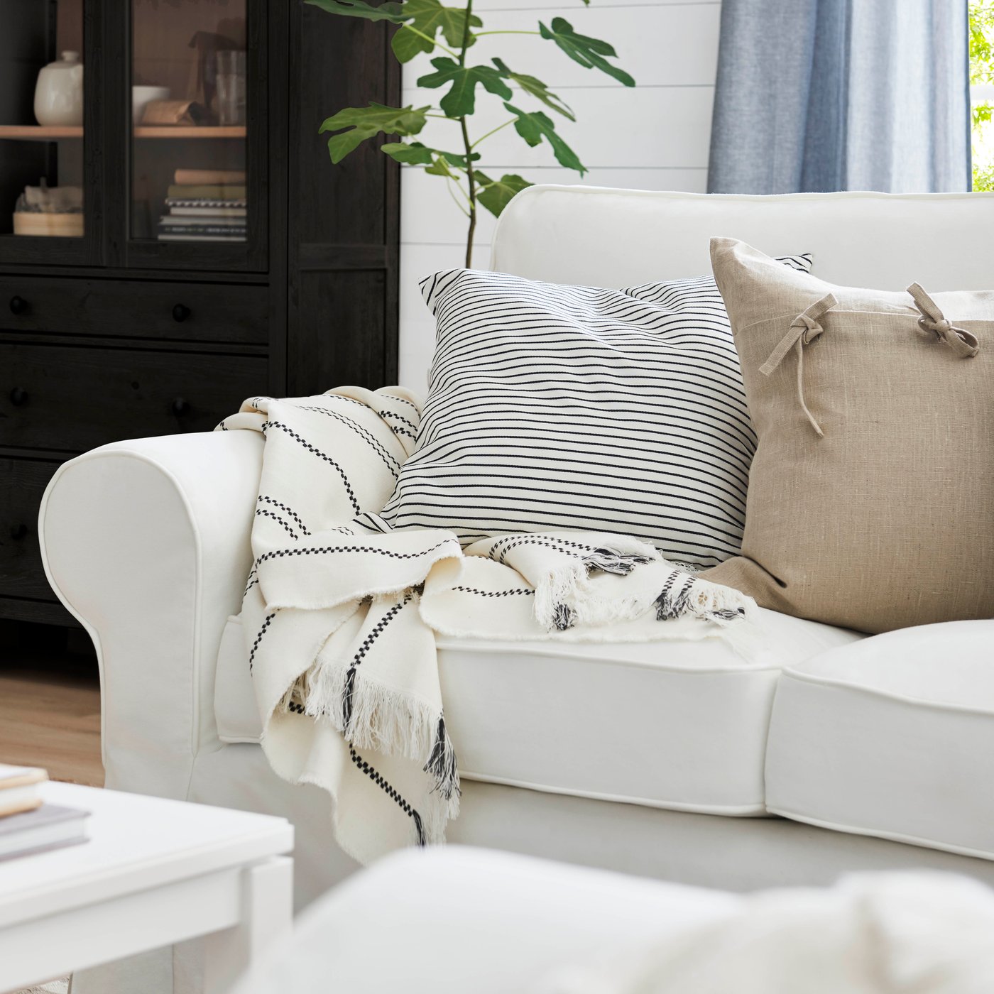 A zoomed in part of a white EKTORP sofa with pillows and a blanket