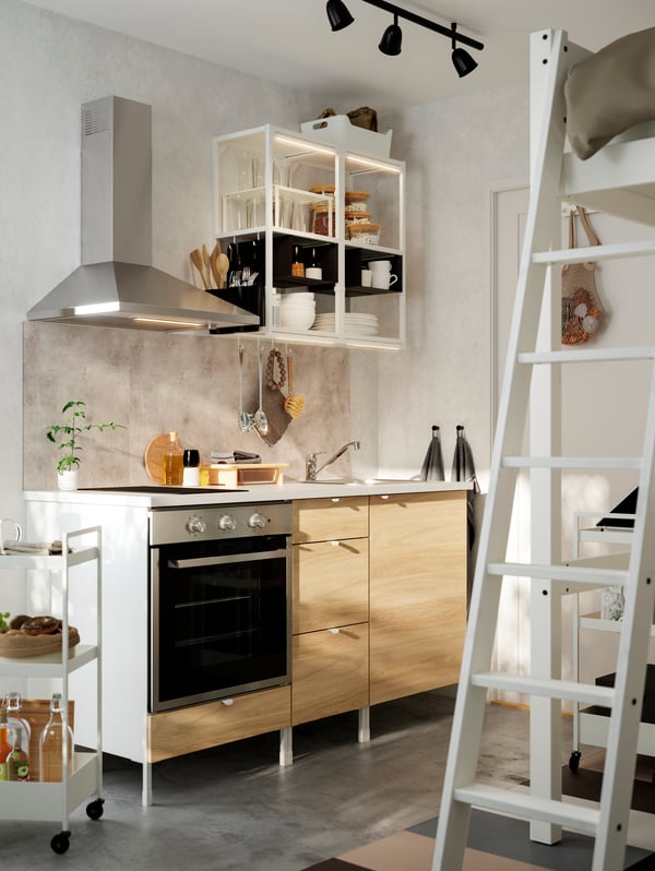 An ENHET kitchen with a wall-mounted extractor hood in stainless steel, open wall storage in white and a white ladder.