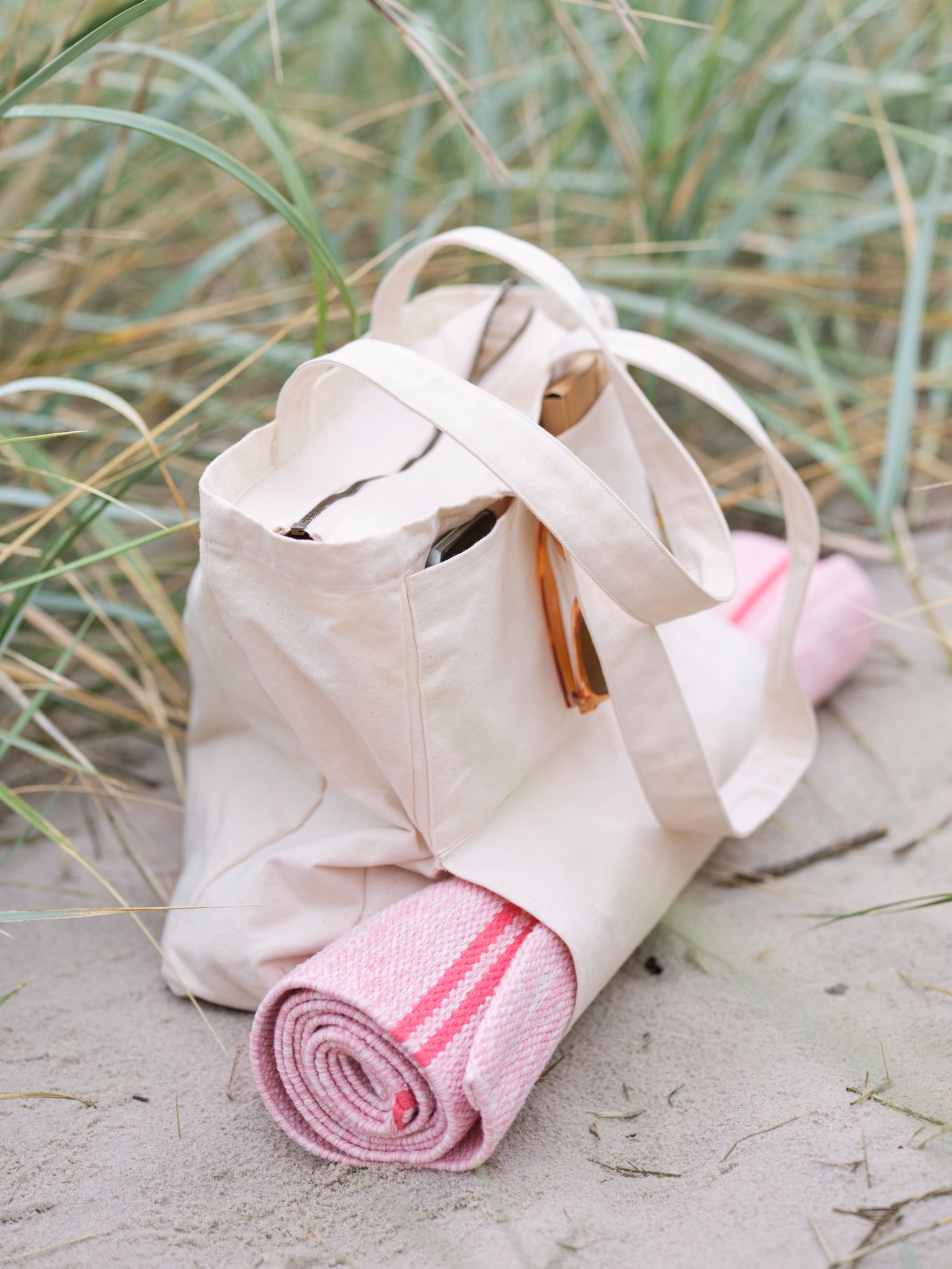 VÅRDANDE cotton canvas bag with zip and rolled yoga rug sitting on sand next to long grasses.