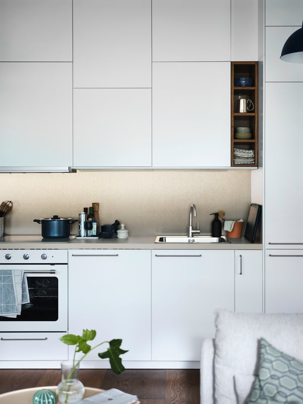 An open plan white METOD kitchen with a beige stone effect/laminate KASKER worktop and a white MATTRADITION forced air oven.