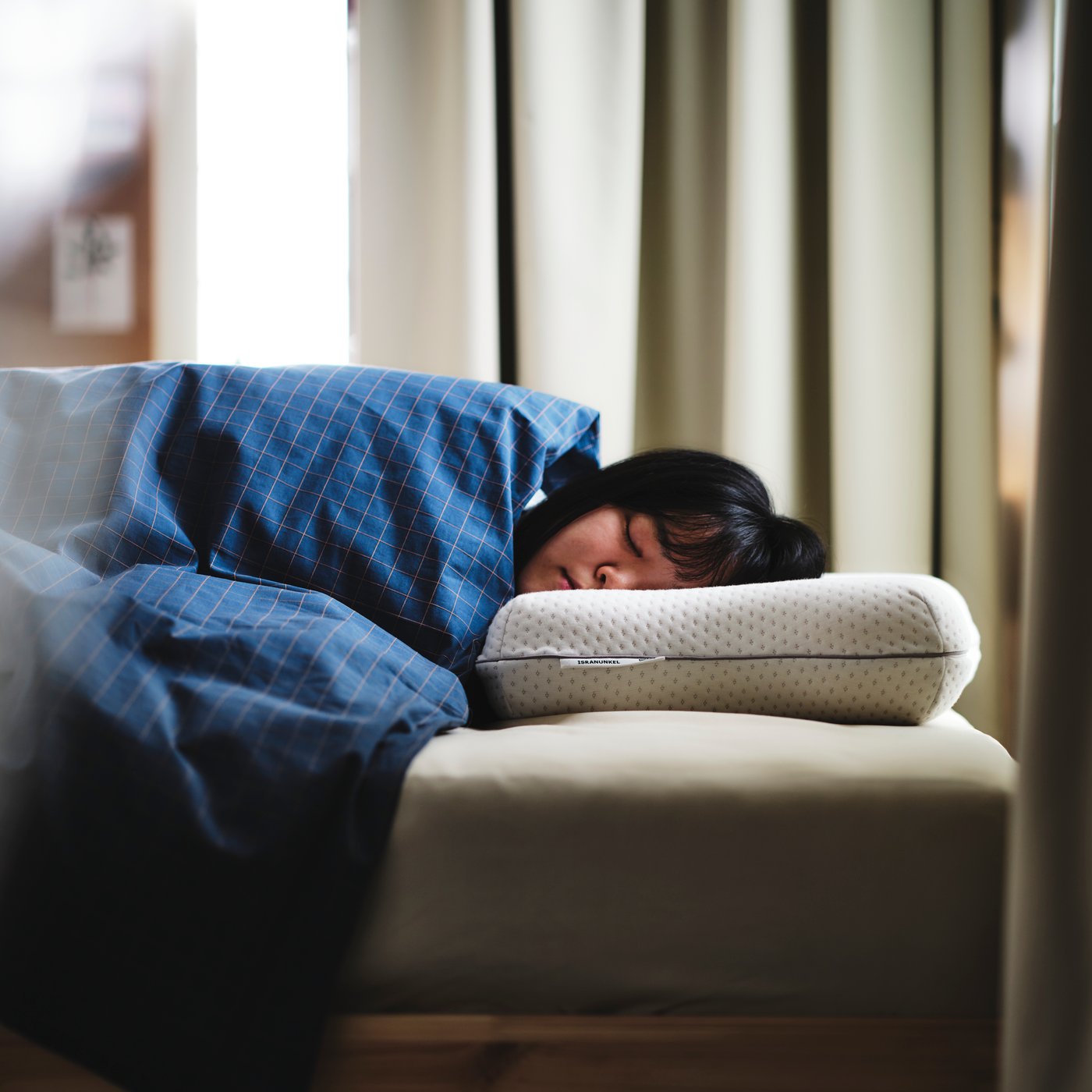 Personne dormant sous du linge de lit DOFTAKLEJA bleu/brun, la tête posée sur un oreiller ergonomique pour couchage multiposition ISRANUNKEL.