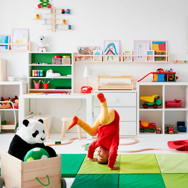 A children's play room with bright green play mats and a girl doing a handstand.