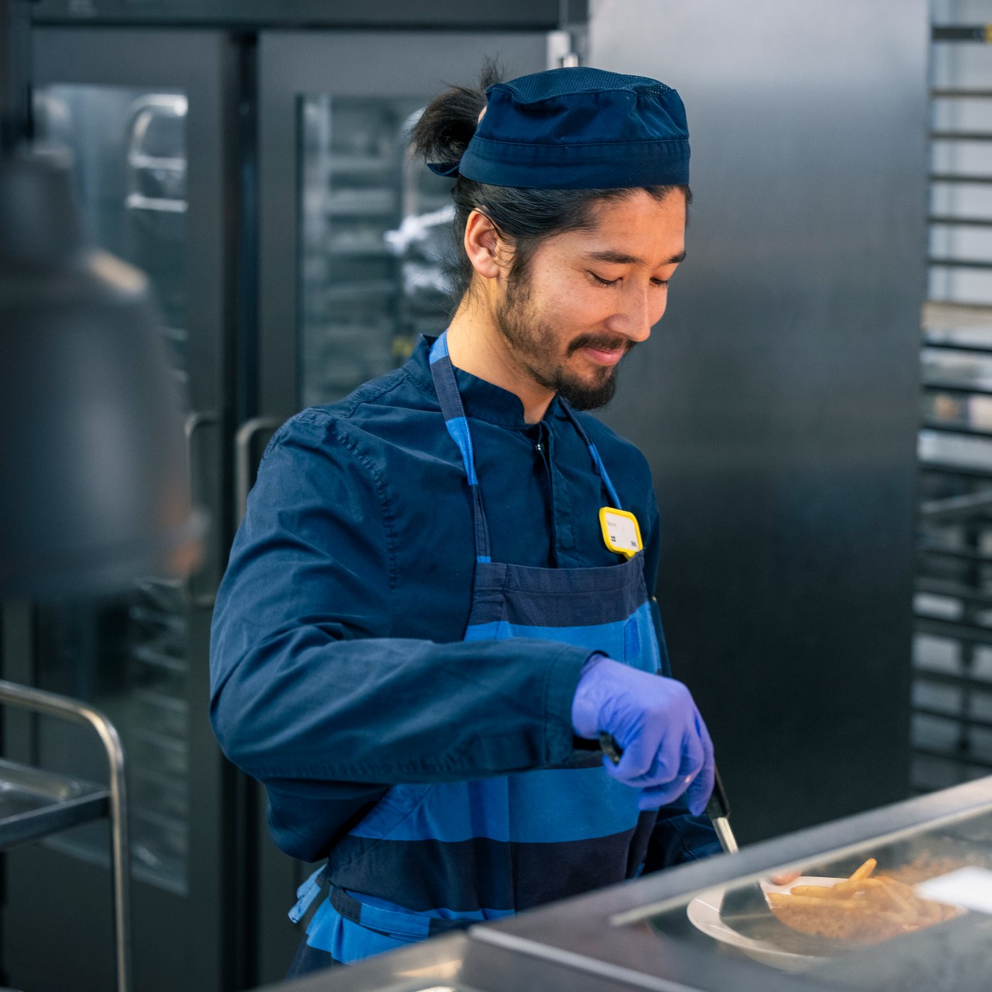 A smiling IKEA co-worker wearing blue workwear and a name badge.