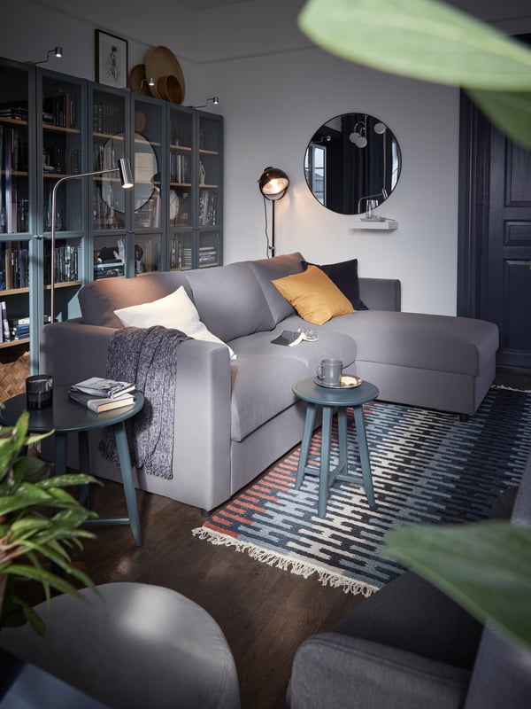 A gray sofa with chaise longue, dark blue-green nesting tables, gray-turquoise bookcases with glass doors, a colorful rug.