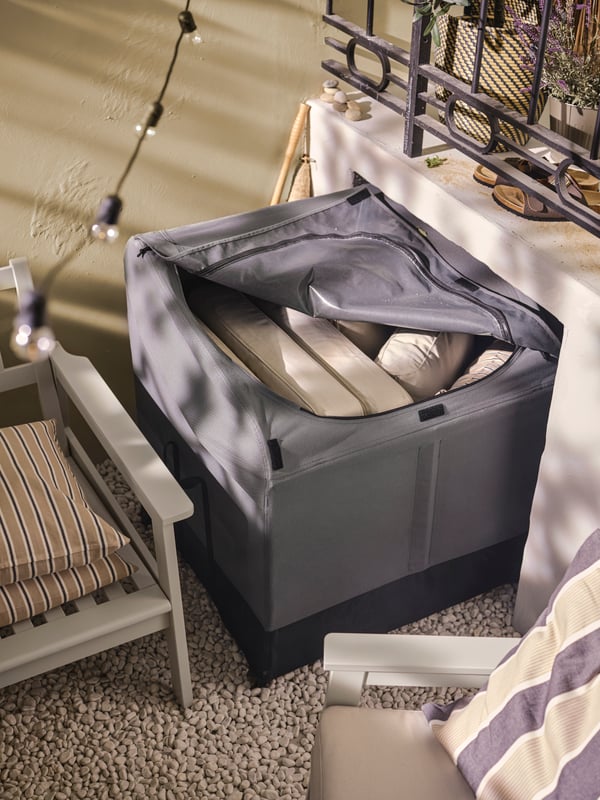 En grå dynbox med beige dynor i på en uteplats. 