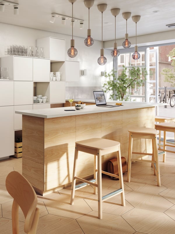 RÖNNINGE Barhocker stehen an einer Bar, über der LED-Lampen hängen. Auf der Bar befinden sich ein Glas Wein, ein Laptop und Schüsseln mit Essen.