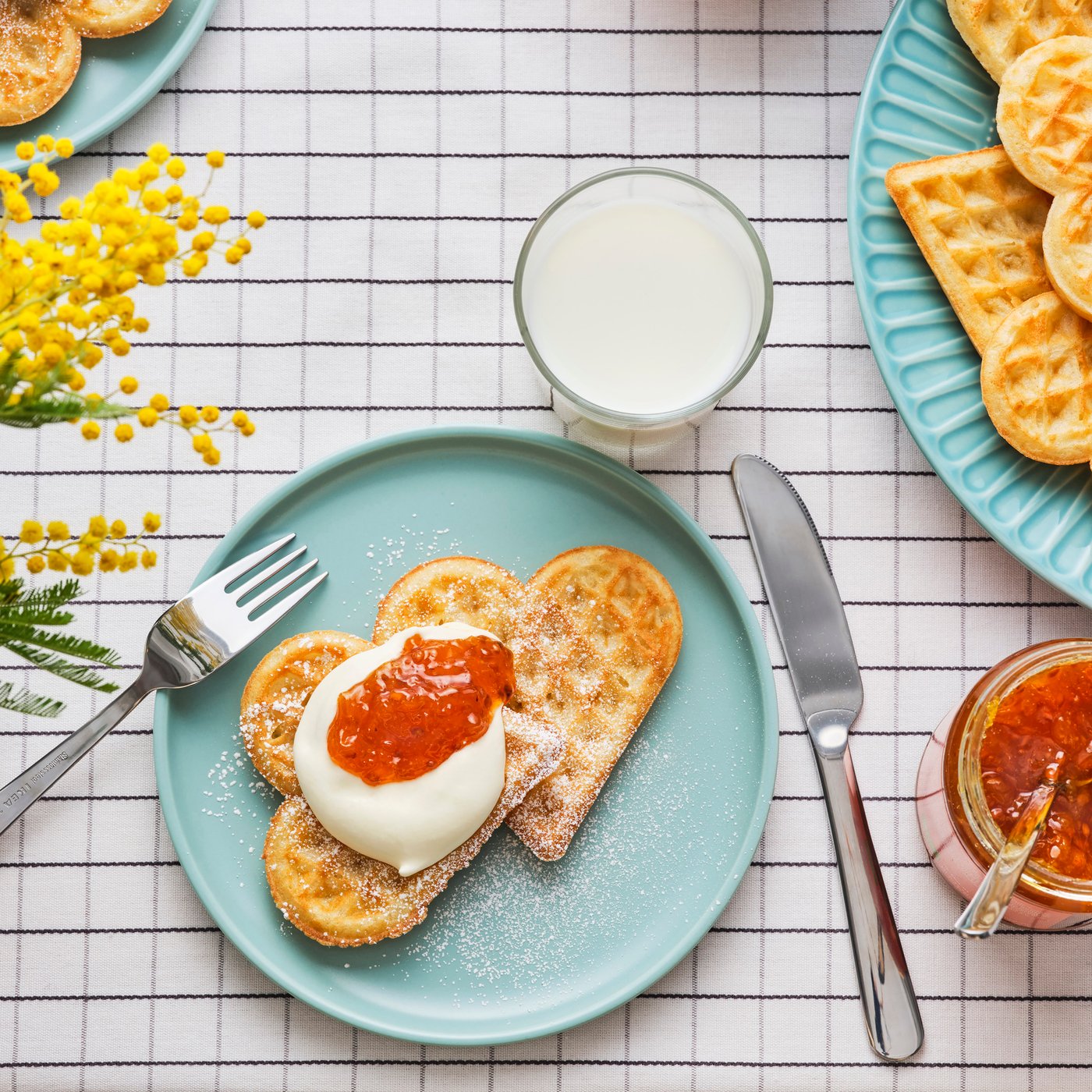 Un plato blanco con un tenedor y cuchilo y dos waffles con crema y mermelada de naranja. El azúcar en polvo se espolvorea encima.