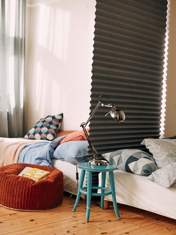 Two single beds placed head to head along a wall, with a dark grey SCHOTTIS block-out pleated blind hanging between them.