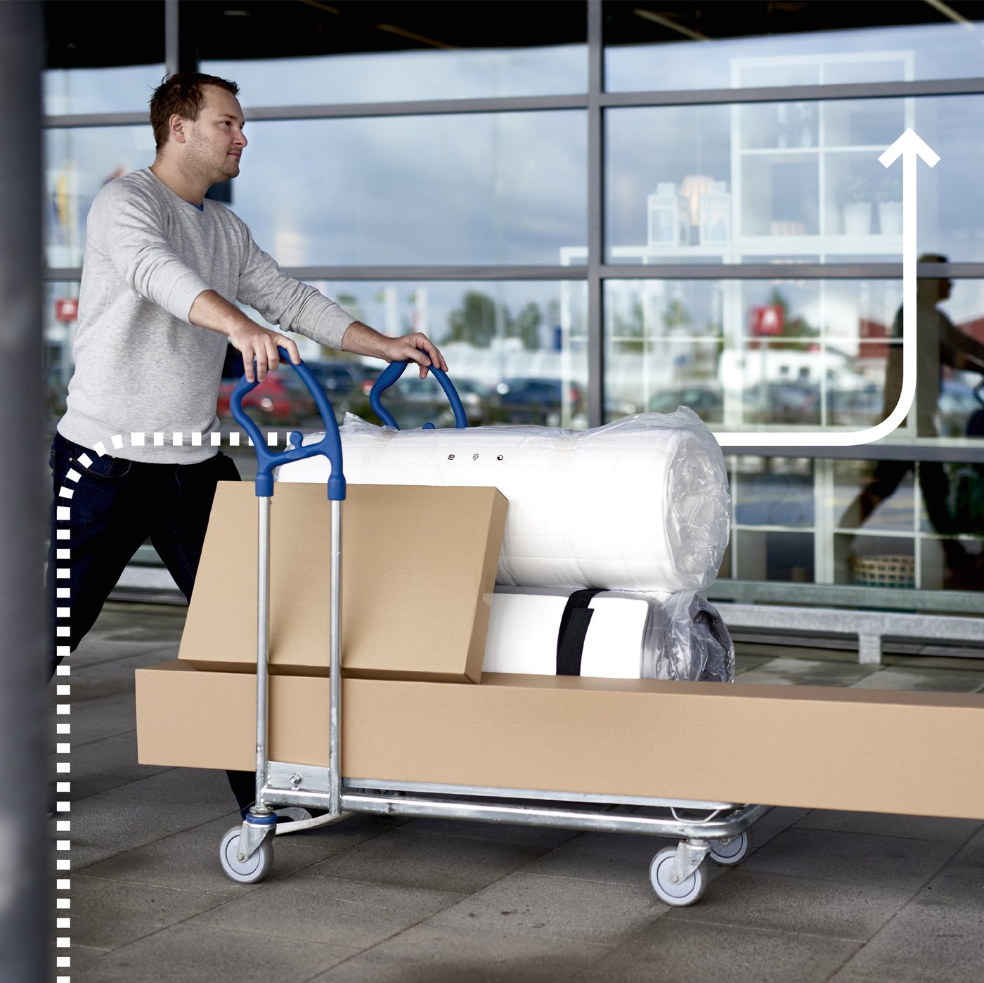 Ein Mann schiebt einen IKEA Lastenwagen voll mit Paketen und Matratzen