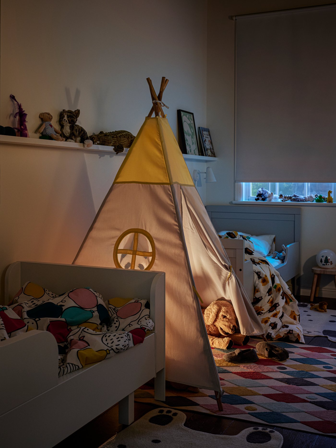 A HÖVLIG children’s tent on a multicolour BUSENKEL rug between two white extendable beds. Picture ledges are on the wall.