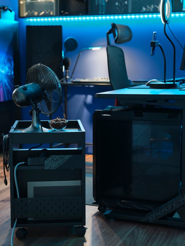 Una cajonera UPPSPEL con un ventilador y accesorios guardados, junto a un soporte para CPU bajo un escritorio gamer UPPSPEL negro.