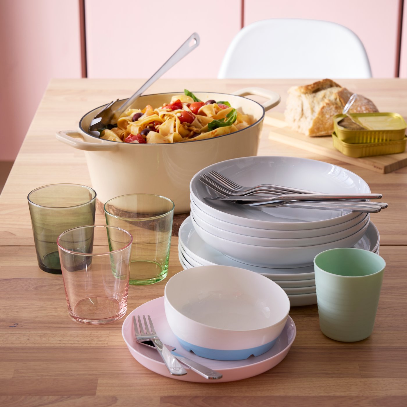 A light yellow VARDAGEN casserole with lid, stacked plates and colourful glasses are on a KARSKÄR extendable dining table.